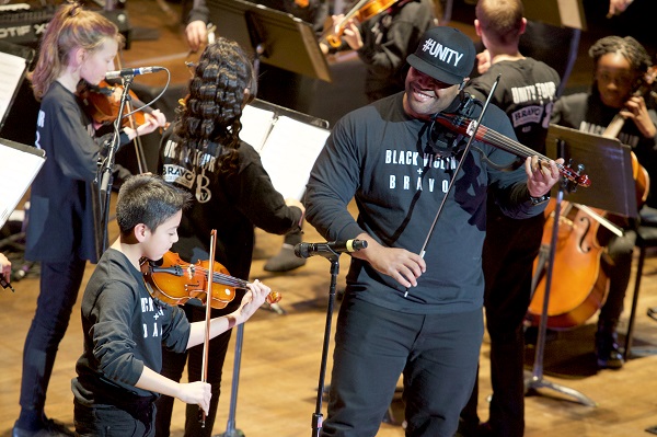 man plays a violin with children on stage